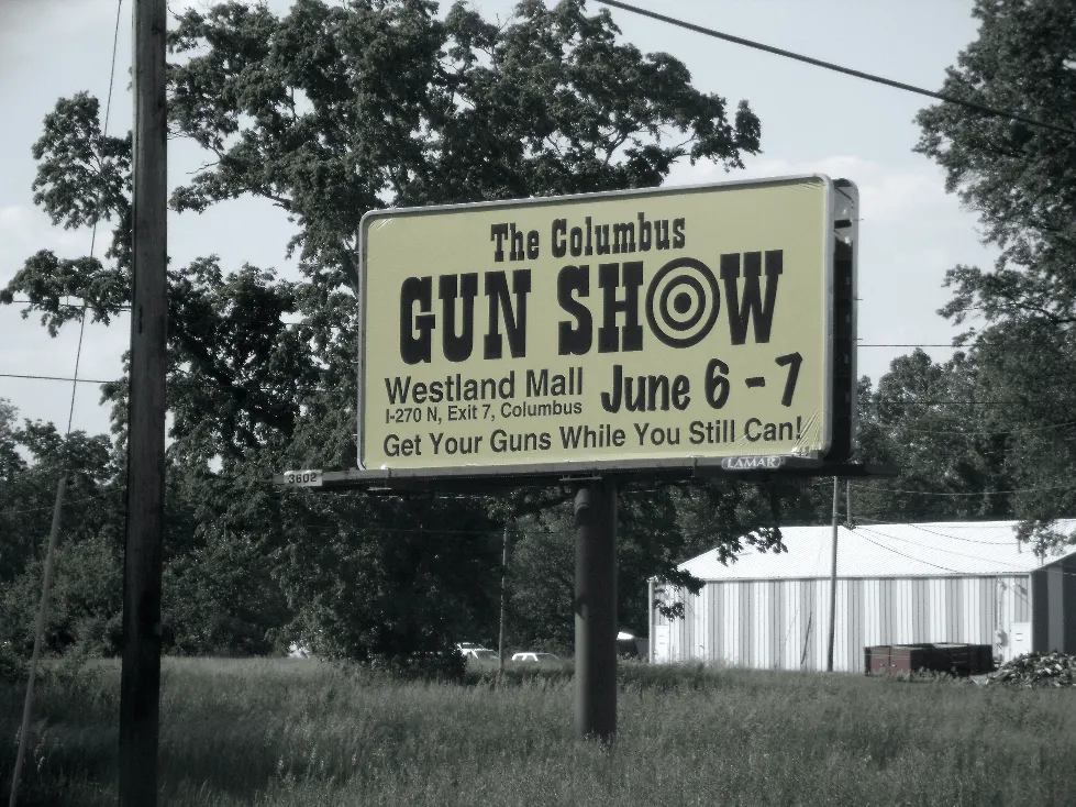 gun show sign in field on billboard