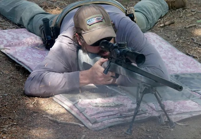 A shooter lying prone on a shooting mat aiming the Springfield Armory Model 2020 Redline rifle at a distant target